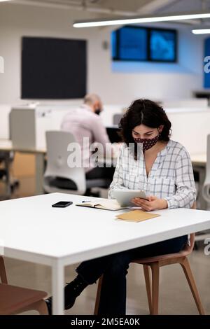 Two young colleagues in masks sitting in the office and working Stock Photo