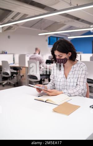 Two young colleagues in masks sitting in the office and working Stock Photo