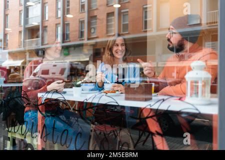 Three young people sitting at a cafe, smiling, and having a warm conversation Stock Photo