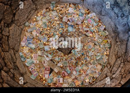 Wish well filled with money both banknotes and coins of different currencies, thrown for luck and to make a wish in medieval Ljubljana Castle, Sloveni Stock Photo