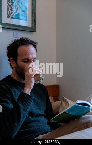 A vertical shot of the Caucasian man drinking coffee and reading a book Stock Photo