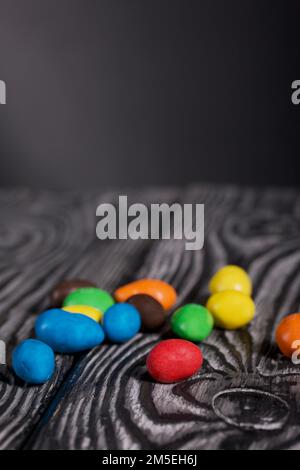 Chocolate candy in multi-colored glaze. Scattered on black pine boards. Close-up. Stock Photo