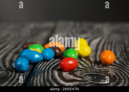 Chocolate candy in multi-colored glaze. Scattered on black pine boards. Close-up. Stock Photo