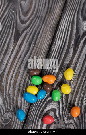 Chocolate candy in multi-colored glaze. Scattered on black pine boards. Stock Photo