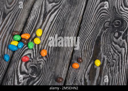 Chocolate candy in multi-colored glaze. Scattered on black pine boards. Stock Photo