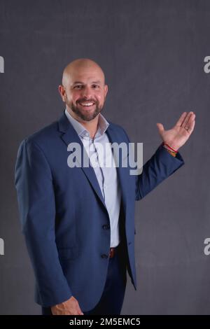 A Studio shot of a young bald businessman in a suit standing against gray background Stock Photo