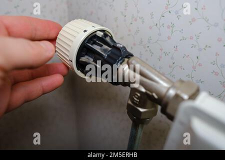Rising heating costs in crisis, man regulates the temperature at home with the heating thermostat to save energy, close up Stock Photo