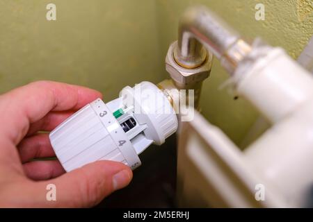 Rising heating costs in crisis, man regulates the temperature at home with the heating thermostat to save energy, close up Stock Photo