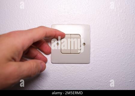 Rising electricity costs in crisis, man switching on the lights at home,  close up by hand Stock Photo