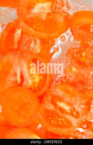 Close-up fresh slices of tomato on white background. Slices of tomato in sparkling water on white background, close-up. Vertical image. Stock Photo