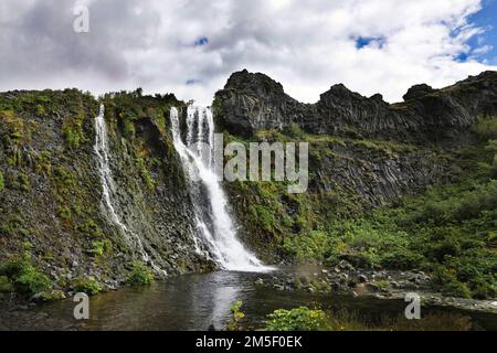 A beautiful view of a waterfall flowing from a cliff under the cloudy sky Stock Photo