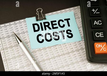 Business concept. On financial reports lies a calculator, a pen and a sticker with the inscription - DIRECT COSTS Stock Photo