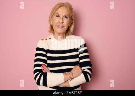 Photo portrait senior woman smiling happy crossed hands in casual striped sweater isolated pastel pink color background. Stock Photo