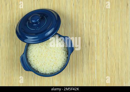 Rice in in blue bowl on a straw background. Vegetarian organic product. Vintage view. Top view. Copy space. Stock Photo