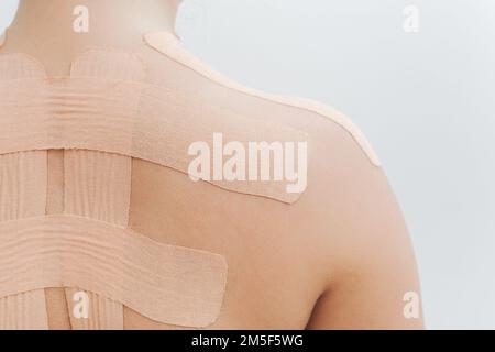 Women's body with kinesio tape on the back and shoulders. Kinesiology taping concept. White background. Close-up view Stock Photo