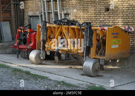 Yellow agriculture soil spading machine for tillage parked near the brick wall of farm building. Stock Photo