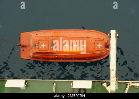 Top view on the orange colour life boat with reflective tape stickers secured with davits and safety hooks. Stock Photo