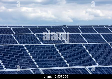A closeup of solar panels in a field under the bright sun and fluffy clouds Stock Photo