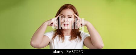 Smart choice. Intrigued thoughtful good-looking assertive redhead creative middle-aged woman touch temples squinting pondering info thinking use Stock Photo