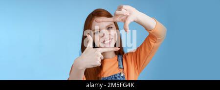 Joyful attractive sincere redhead young girl searching inspiration find perfect angle take good shot make hand frames look through delighted amused Stock Photo