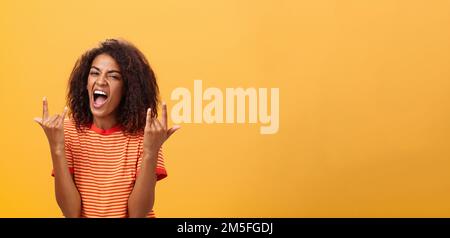 Waist-up shot of amazed happy stylish african american woman feeling awesome rocking on party yelling from joy and satisfaction showing rock n roll Stock Photo