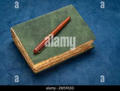 retro leather-bound journal with decked edge handmade paper pages and a stylish pen on a textured blue bark paper, journaling concept Stock Photo