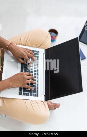 Unrecognizable woman working at home with a laptop on a floor. Writing an email. Stock Photo