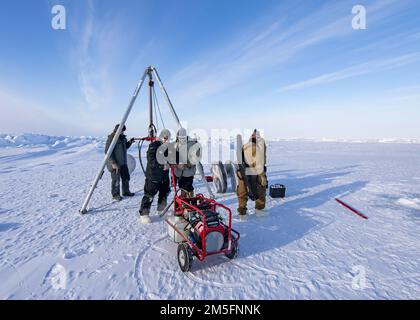BEAUFORT SEA, Arctic Circle (March 14, 2022) – Members of Naval Undersea Warfare Center Newport and Arctic Submarine Laboratory drill a hole in the ice to prepare for retrieving a test torpedo during Ice Exercise (ICEX) 2022. ICEX 2022 is a three-week exercise that allows the Navy to assess its operational readiness in the Arctic, increase experience in the region, advance understanding of the Arctic environment, and continue to develop relationships with other services, allies, and partner organizations. Stock Photo