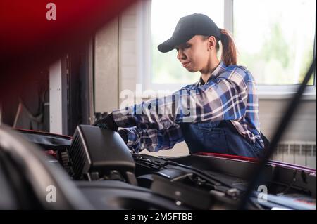 Caucasian female auto mechanic changes the engine air filter in the car. Stock Photo