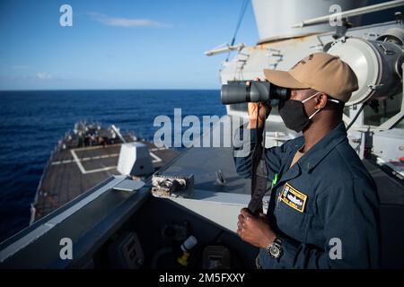 PHILIPPINE SEA (March 15, 2022) Ensign Botha Nzinga, from Kinshasa, D.R. Congo, monitors surface contacts from the bridge wing aboard the Arleigh Burke-class guided-missile destroyer USS Dewey (DDG 105) while conducting routine operations underway in the U.S. 7th Fleet area of responsibility. Dewey is assigned to Destroyer Squadron (DESRON) 15 and is underway supporting a free and open Indo-Pacific. CTF 71/DESRON 15 is the Navy’s largest forward-deployed DESRON and the U.S. 7th Fleet’s principal surface force. Stock Photo