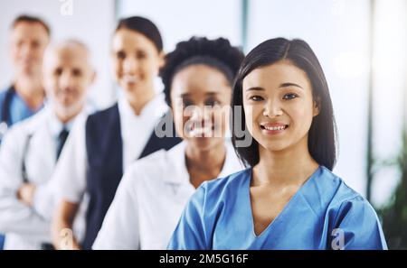 Theyre lining up to help. Cropped portrait of an attractive young female doctor standing at the front of a queue of medical professionals. Stock Photo