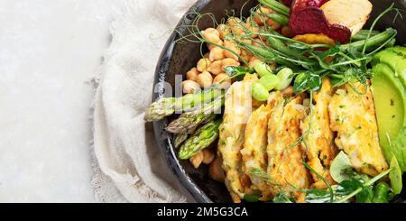 Healthy vegan lunch bowl. Avocado, chickpeas, cutlet, vegetable chips, salad and asparagus on a light background. Top view. Panorama with copy space. Stock Photo