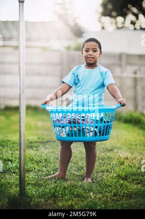 I always help do the chores. Portrait of a young boy holding a basket of laundry outdoors. Stock Photo