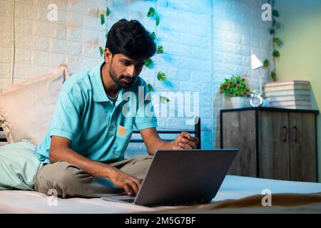 young man busy woking on laptop uring night on bed - concept of over working, work from home and project deadline Stock Photo