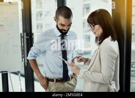 You need to check this out. two colleagues using a digital tablet while standing together in an office. Stock Photo
