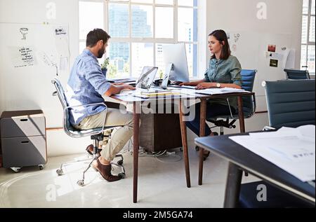 Working hard to turn their startup into a success. colleagues working on their computers at a desk in an open plan office. Stock Photo