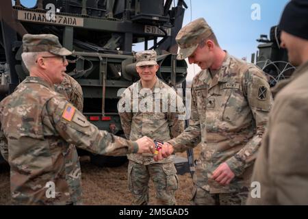 Maj. Gen. Greg Brady, Commanding General of the 10th Army Air and Missile Defense Command, presents a commander’s coin for excellence to Spc. Samuel Backes, an air defender assigned to the 5th Battalion, 7th Air Defense Artillery Regiment during a site visit in Poland on March 16, 2022. Stock Photo