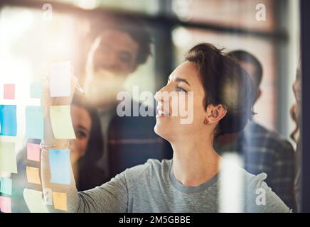 Shes on to something...coworkers using sticky notes on a glass wall during an office meeting. Stock Photo