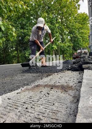 Asian male worker holding cart and pile of asphalt on road in Indonesia Stock Photo