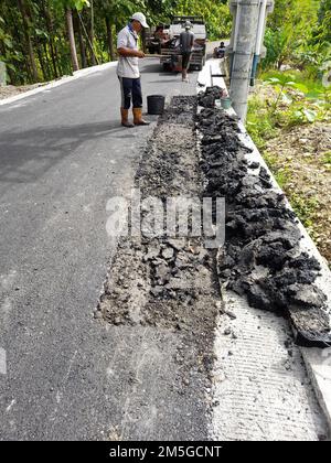 Asian male worker holding cart and pile of asphalt on road in Indonesia Stock Photo