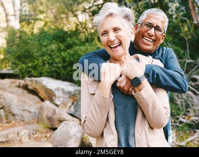 Hiking, laugh and romance with a senior couple hugging while in the woods or nature forest together in summer for a hike. Fun, joke and bonding with a Stock Photo