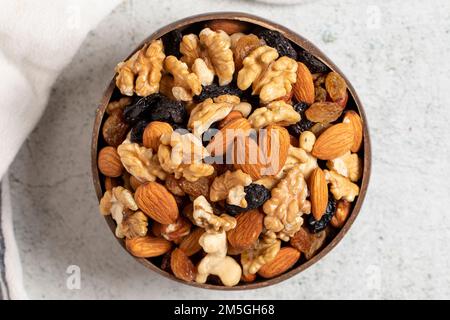 Raw mixed nuts on gray background. Walnuts, almonds, hazelnuts and raisins in a coconut bowl. Top view Stock Photo