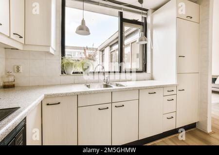 a kitchen area with white cabinets and black trim around the window simh is in front of the sink Stock Photo