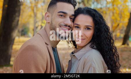 Close-up portrait outdoors Hispanic ethnic multiracial couple in love in autumn park looking at camera guy man and girl woman smiling stand close to Stock Photo