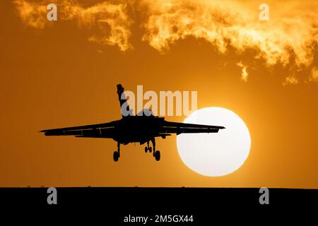 Fighter jet landing at sunset with orange sky and large setting sun after a combat mission. Tornado Fighter Bomber Stock Photo