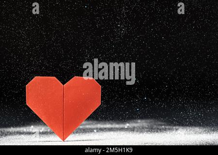 Postcard for Valentinan Day. A red heart on a black background, sparkles falling, snow, a place for text. Stock Photo