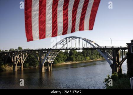 Selma to Montgomery March Byway - Flag Framing Edmund Pettus Bridge. The red and white stripes of the American flag hang over a view of the Edmund Pettus Bridge crossing the Alabama River in the distance. Location: Selma, Alabama Stock Photo