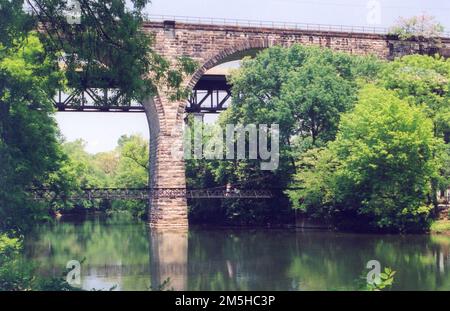 Brandywine Valley Scenic Byway - Stone Bridge Over the Brandywine River. In Brandywine River Park, people stroll over the lower pedestrian bridge while the upper stone bridge is reflected in the clear water of the Brandywine River. Location: Brandywine River Park, Wilmington, Delaware Stock Photo