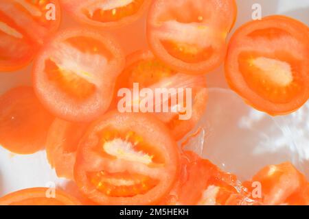 Tomato close-up in liquid with bubbles. Slices of red ripe tomato in water. Close-up fresh slices of red tomato on white background Stock Photo
