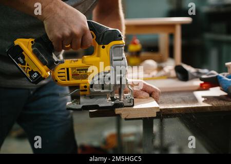 Close up on hand of unknown carpenter working with an electric jigsaw cutting wood with saw. Stock Photo
